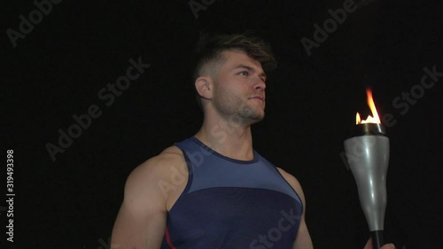 Male Athlete Holding the Olympic Torch. Black Background. Super slow motion. Rotating around photo