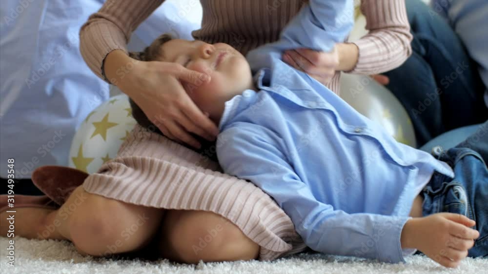 Little son is lying on mother's knees, on the floor while mom is stroking him, close-up. Father playing with children on the background