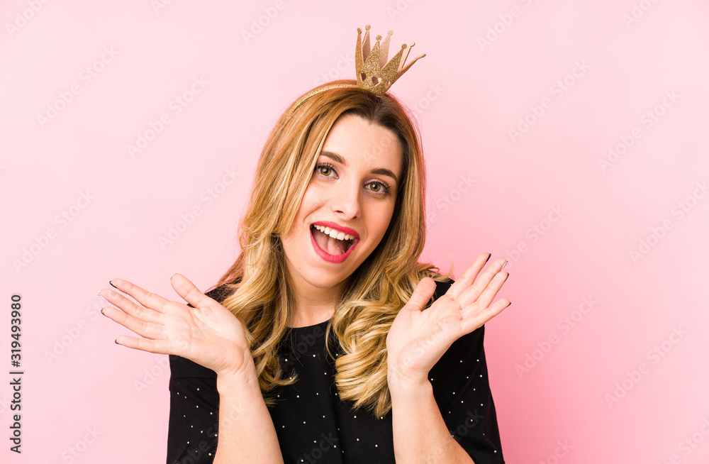 Young blonde woman wearing a crown isolated receiving a pleasant surprise, excited and raising hands. Young blonde woman wearing a crown isolated receiving a pleasant surprise, excited and raising hands.