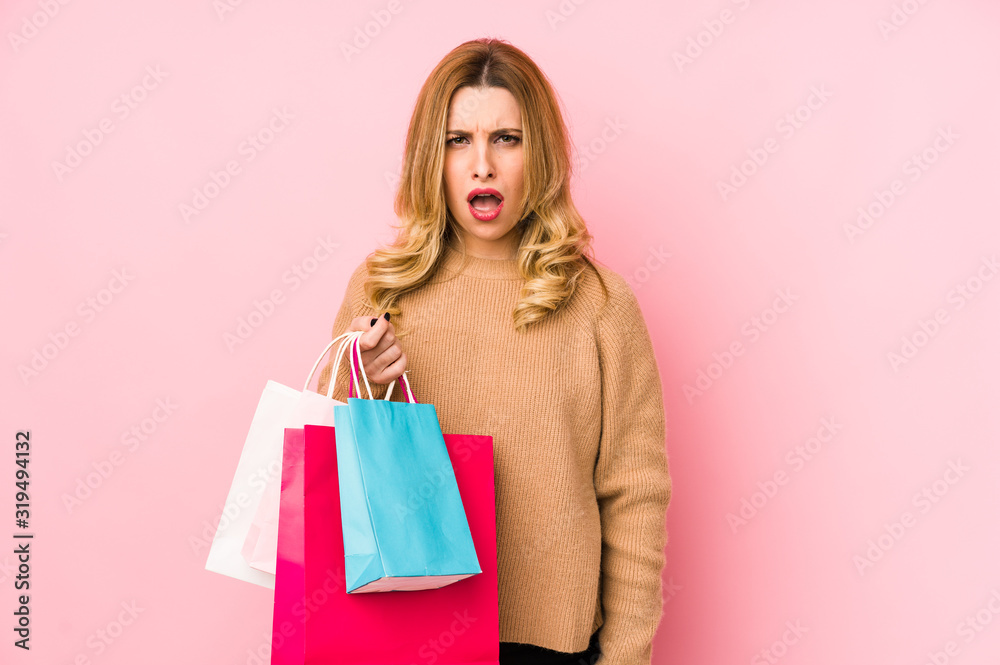 Young blonde woman holding shopping bags isolated screaming very angry and aggressive.
