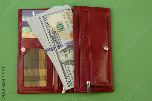 Red wallet or purse with a stack of one hundred dollars cash isolated on a green background. Business and finance concept. With copy space for text.