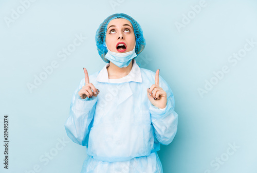 Young surgeon woman isolated pointing upside with opened mouth. © Asier