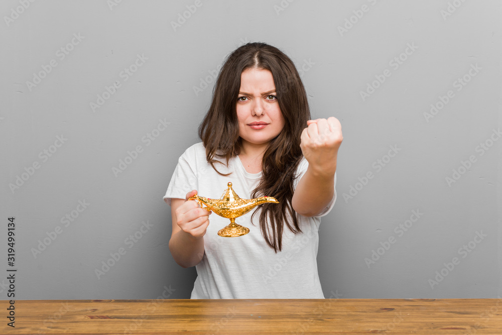 Young plus size curvy woman holding a magic lamp showing fist to camera, aggressive facial expression. Young plus size curvy woman holding a magic lamp showing fist to camera, aggressive facial expression.