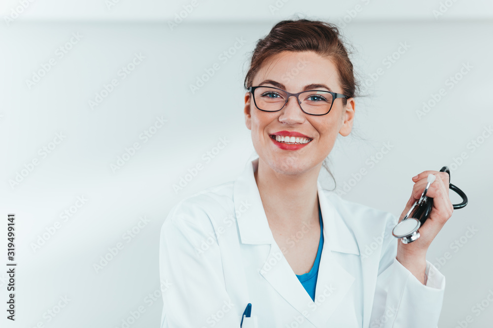 Smiling young female doctor holding stethoscope in hospital office. Dentist standing in ward.