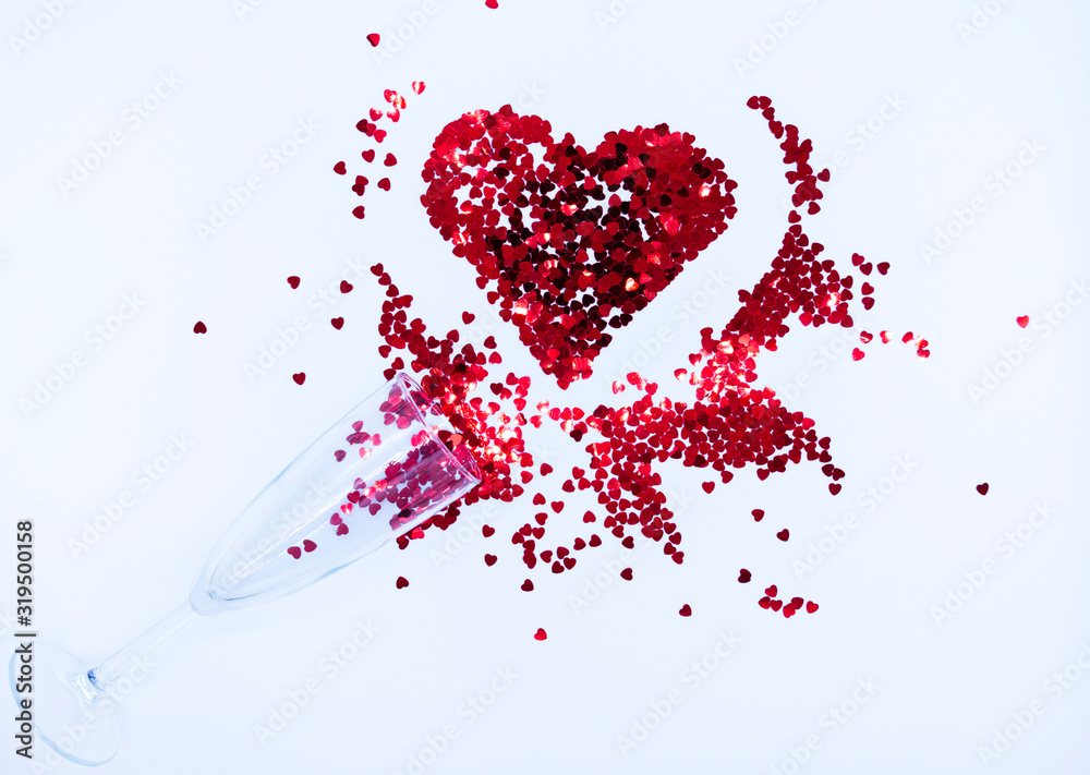 Champagne glass with red sequins scattered in the form of a heart on a white backdrop. Background for Valentine's day. Top view. Flat lay. Champagne glass with red sequins scattered in the form of a heart on a white backdrop. Background for Valentine's day. Top view. Flat lay.