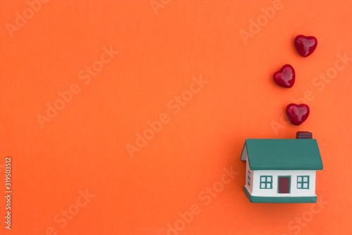 A little house, red hearts fly out of the pipe on an orange background. The concept of happiness, joy, love in your home, buying, selling, renting real estate, mortgage