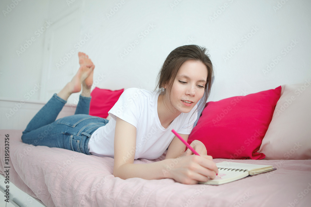 Young woman writing something in the notebook on the bed. Peaceful atmosphere. Young woman writing something in the notebook on the bed. Peaceful atmosphere.