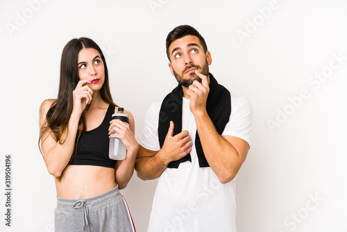 Young caucasian fitness couple isolated looking sideways with doubtful and skeptical expression.