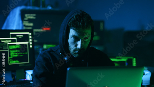 Portrait of dangerous computer hacker working on computer scheming cyber attack on server in the office at night.