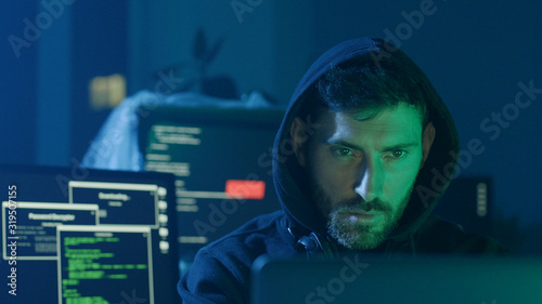 Portrait of confident programmer or internet hacker in hoodie looking at computer screen and smiling.