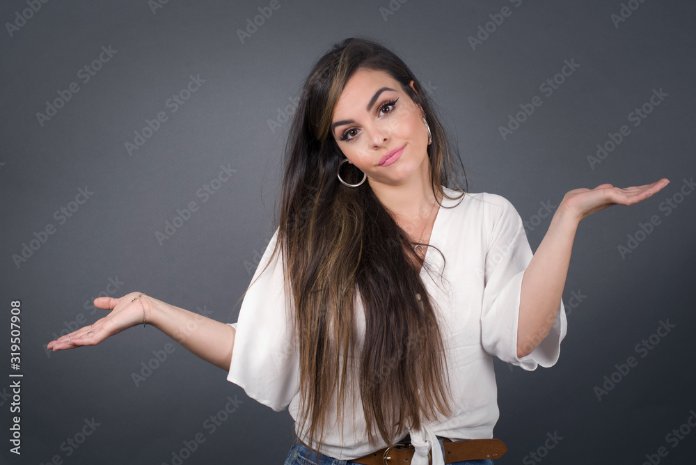Beautiful woman doubt expression, confuse and wonder concept, uncertain future shrugging shoulders, standing against gray Wall.