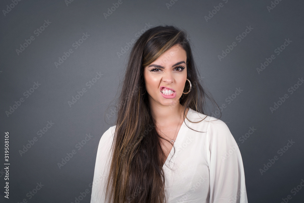 Mad crazy woman clenches teeth angrily, being annoyed with coming noise, dressed in fashionable clothes, isolated over gray background. Negative feeling concept. Mad crazy woman clenches teeth angrily, being annoyed with coming noise, dressed in fashionable clothes, isolated over gray background. Negative feeling concept.