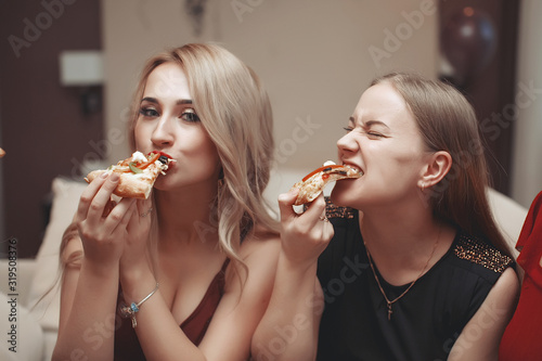 Friends taking slices of tasty pizza from plate  close up view. Women partying in hotel room  eating junk food and having fun