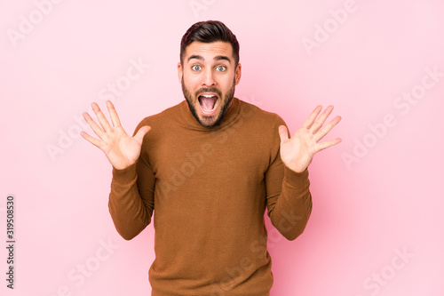Young caucasian man against a pink background isolated celebrating a victory or success, he is surprised and shocked. © Asier