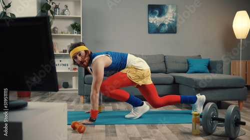 LOS ANGELES, CALIFORNIA, 10 OCTOBER, 2019: Handsome concentrated sportsman in retro outfit training abs at home. Motivated athlete man trying to get fit exercising on mat and watching sport videos.