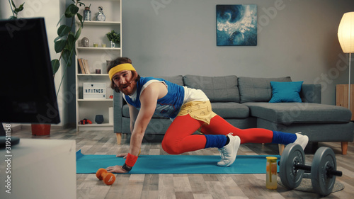 Handsome concentrated sportsman in retro outfit training abs at home. Motivated athlete man trying to get fit exercising on mat and watching sport videos.