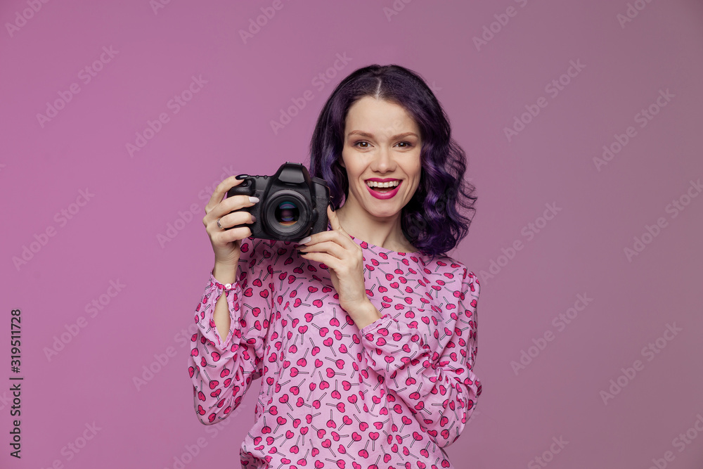 Beautiful woman with violet hair holds a reflex camera in studio pink background. Professional photographer. Learn to take pictures. Astonishment smile expression emotion positive. Full-frame Lens Beautiful woman with violet hair holds a reflex camera in studio pink background. Professional photographer. Learn to take pictures. Astonishment smile expression emotion positive. Full-frame Lens
