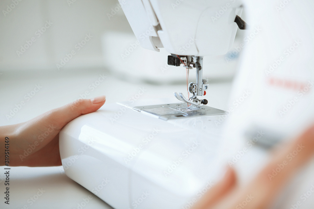 Close up hands of young woman seamstress sitting and sews on sewing machine in studio