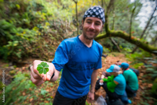 A man stands on a trail smiling holding a four-leaf clover while backpacking the Lost Coast Trail in Sinkyone Wilderness State Park in Northern California.
