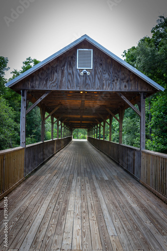 A wooden, covered bridge with green trees in the background. © Leon