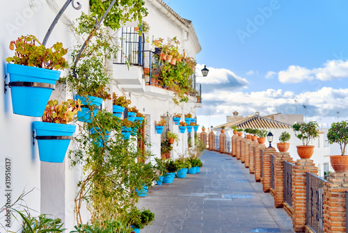 Fototapeta Naklejka Na Ścianę i Meble -  Idyllic scenery empty picturesque street of small white-washed village of Mijas. Path way decorated with hanging plants in bright blue flowerpots, Costa del Sol, Andalusia, Province of Málaga, Spain.