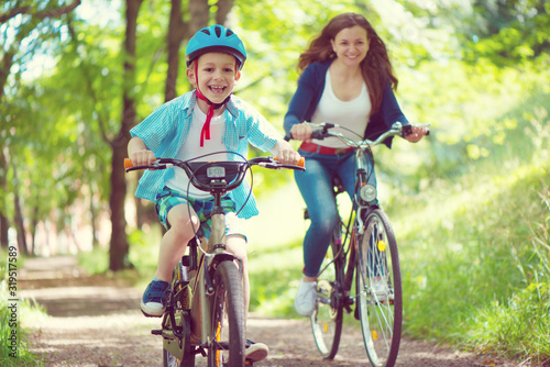 Happy young mother and son ride on bikes in park
