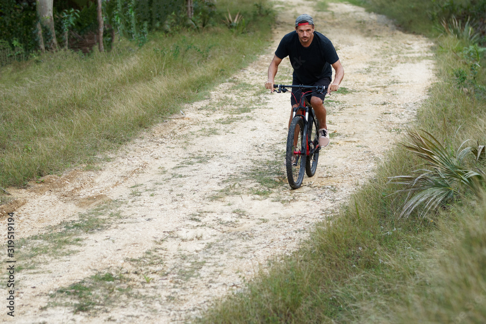 Naklejka premium A casually dressed man rides a mountain bike on a rural road.