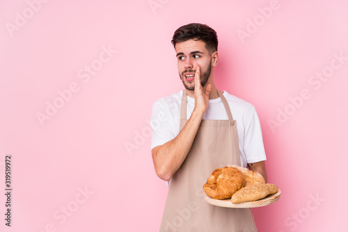 Young caucasian baker man isolated is saying a secret hot braking news and looking aside