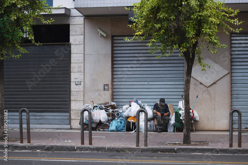 Male isolated homeless wearing a brown hat sitting on the pedestrian.