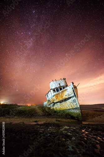 A shipwreck is illuminated at night with the Milky Way and stars in the sky in the town of Iverness in the Point Reyes National Seashore, California. photo