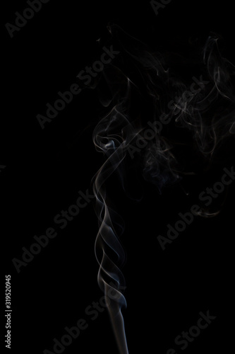 Delicate column of smoke from incense stick isolated on black background, selective focus