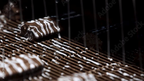 Machine pouring liquid on candies. Conveyor belt with brown sweets. Production of high-quality dessert. Under a flow of chocolate.