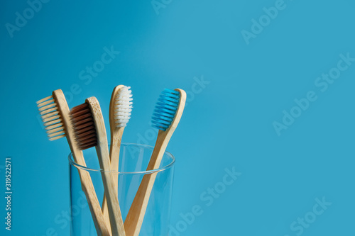 Wooden toothbrushes with a glass cup on a blue background with copy space. Environmental awareness  pollution and zero waste concept. Closeup.