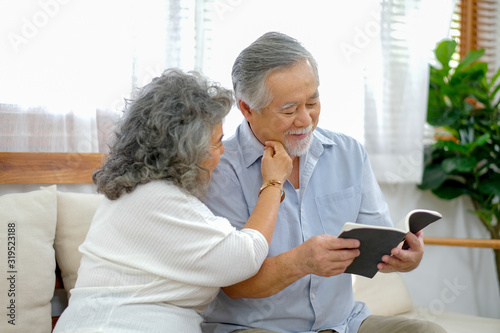 Old woman touch old man face during read book in the living room and they look happy together.