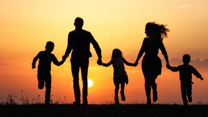 Silhouettes of happy family holding the hands in the meadow during sunset.