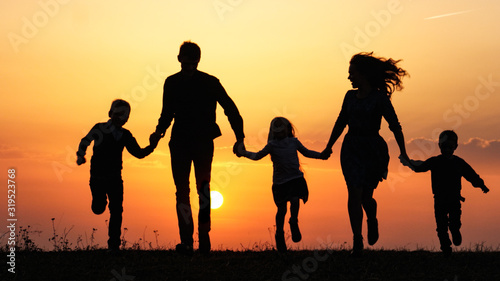 Silhouettes of happy family holding the hands in the meadow during sunset.
