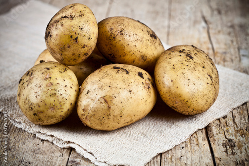 Fresh organic dirty potatoes heap closeup on linen tablecloth on rustic wooden background. photo