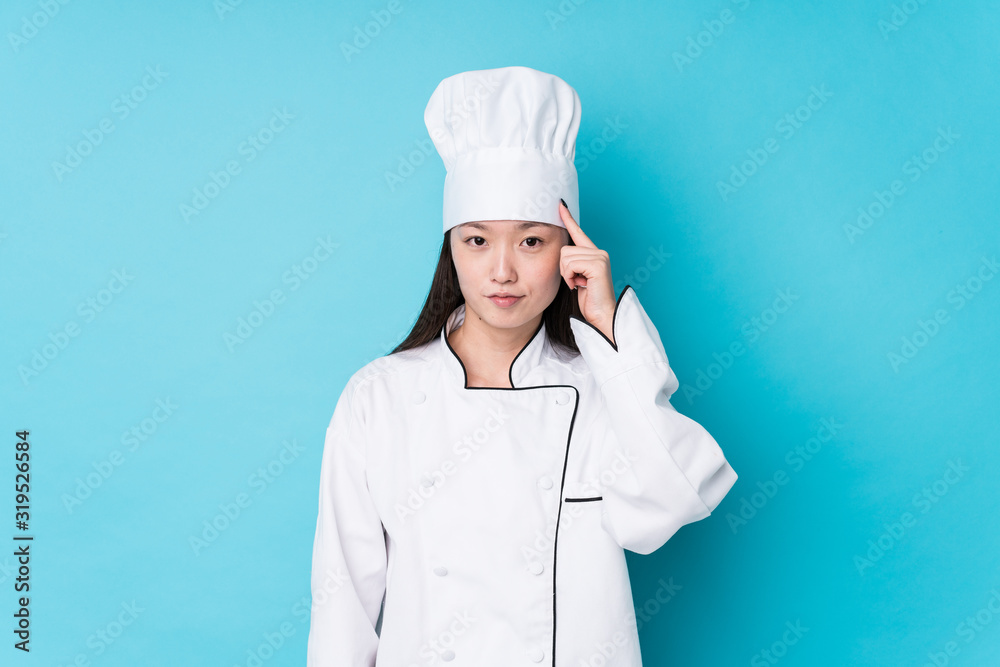 Young chinese chef woman isolated pointing temple with finger, thinking, focused on a task. Young chinese chef woman isolated pointing temple with finger, thinking, focused on a task.