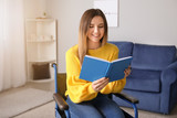Handicapped young woman in wheelchair reading book at home