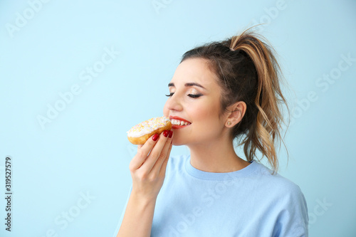 Beautiful young woman eating donut on color background