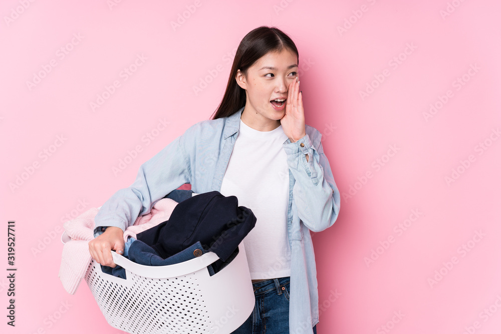 Young chinese woman picking up dirty clothes isolated shouting and holding palm near opened mouth. Young chinese woman picking up dirty clothes isolated shouting and holding palm near opened mouth.