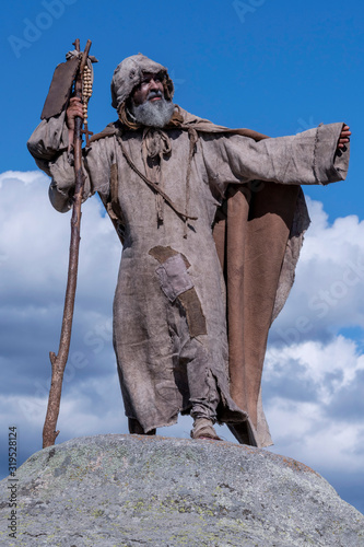 Beggar, ragged, holding on a stick, climbed on a rock in the countryside photo