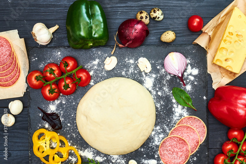 Pizza dough with ingredients on a dark background.