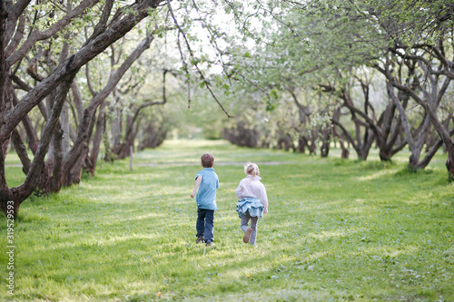 Back view of little boy and girl running side by side on a meadow