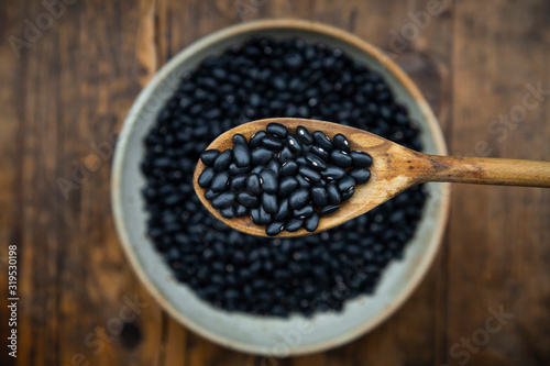 Overhead view of spoon and bowl of black bean on wooden table photo