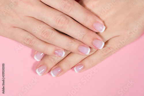 Closeup top view photo of two female hands with beautiful manicure. Fingernails painted with pastel pink and white colors.