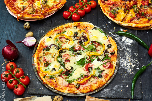 Pizza with mozzarella cheese, tomatoes, mushrooms, peppers, herbs on a dark wooden background.