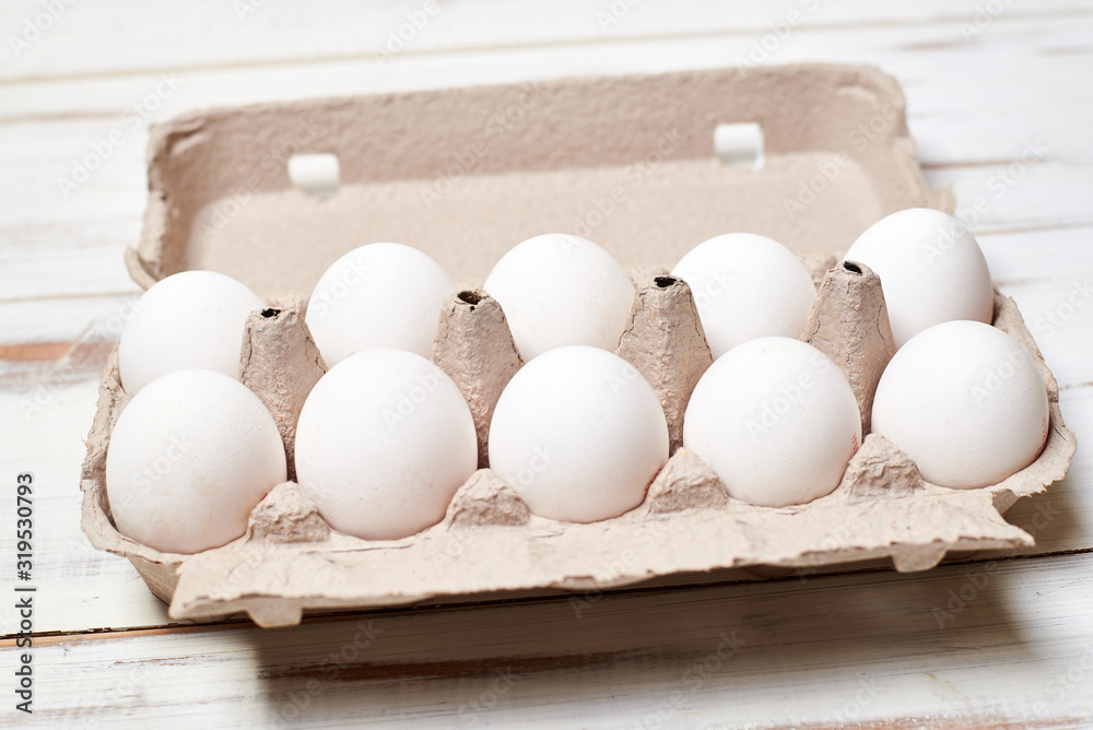 White chicken eggs in a tray on a light wooden background. White chicken eggs in a tray on a light wooden background.