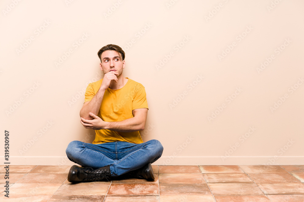 Young caucasian man sitting on the floor isolated relaxed thinking about something looking at a copy space. Young caucasian man sitting on the floor isolated relaxed thinking about something looking at a copy space.