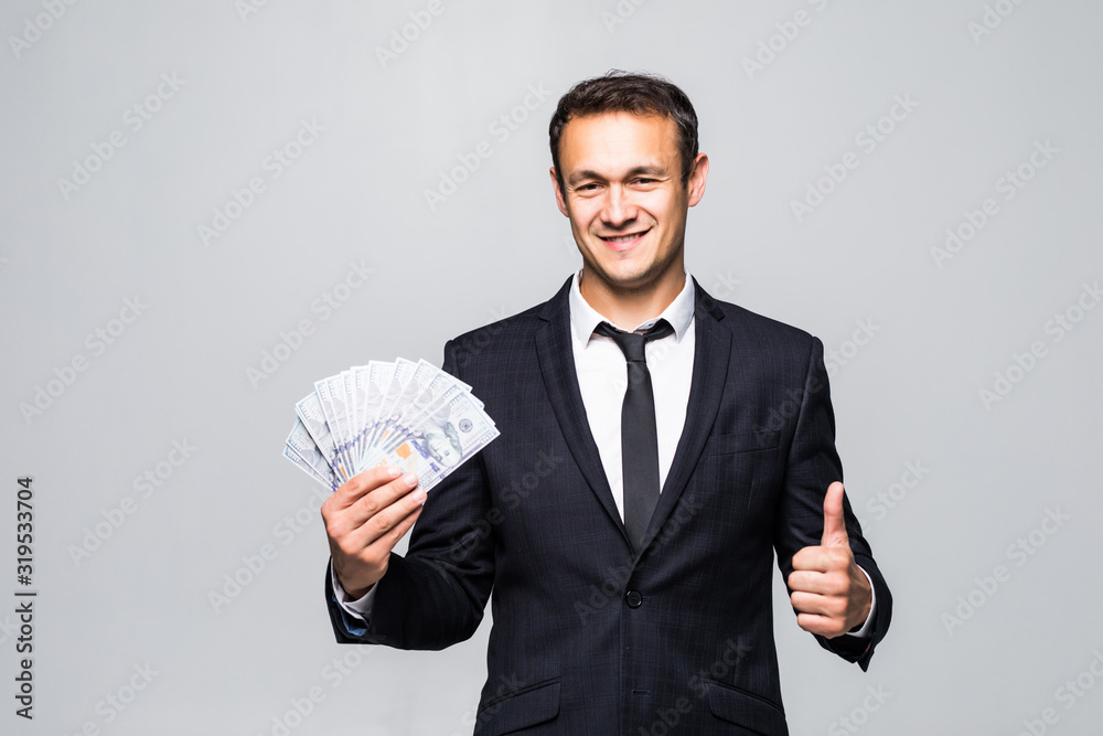 Confident young business man holding dollars banknotes in classic suit shirt tie posing isolated on grey background. Confident young business man holding dollars banknotes in classic suit shirt tie posing isolated on grey background.